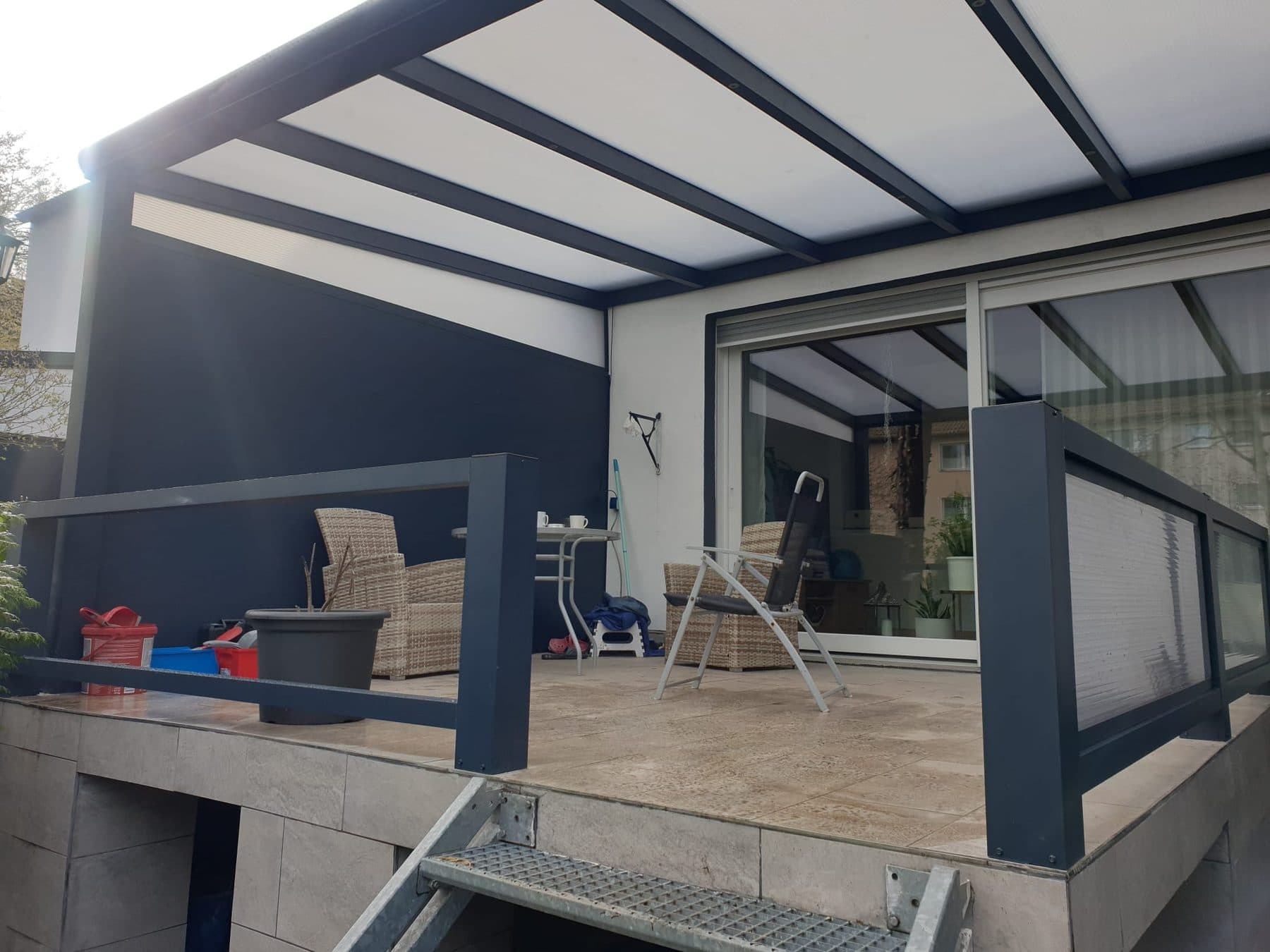 Sous la toiture en polycarbonate opale : terrasse carrelée, garde-corps anthracite et baie vitrée