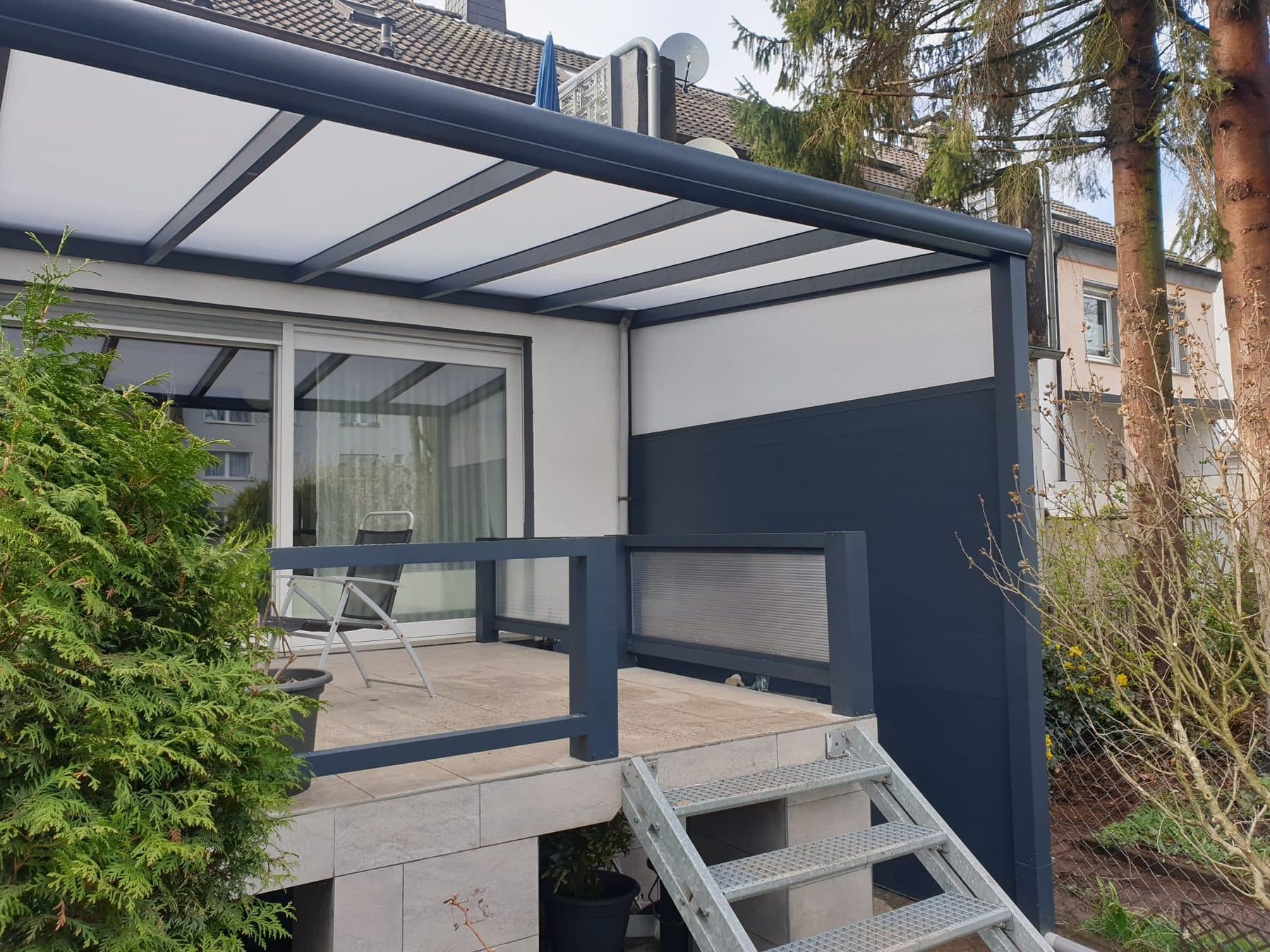 Angle de la pergola avec la paroi pleine anthracite et l'escalier métallique vers le jardin