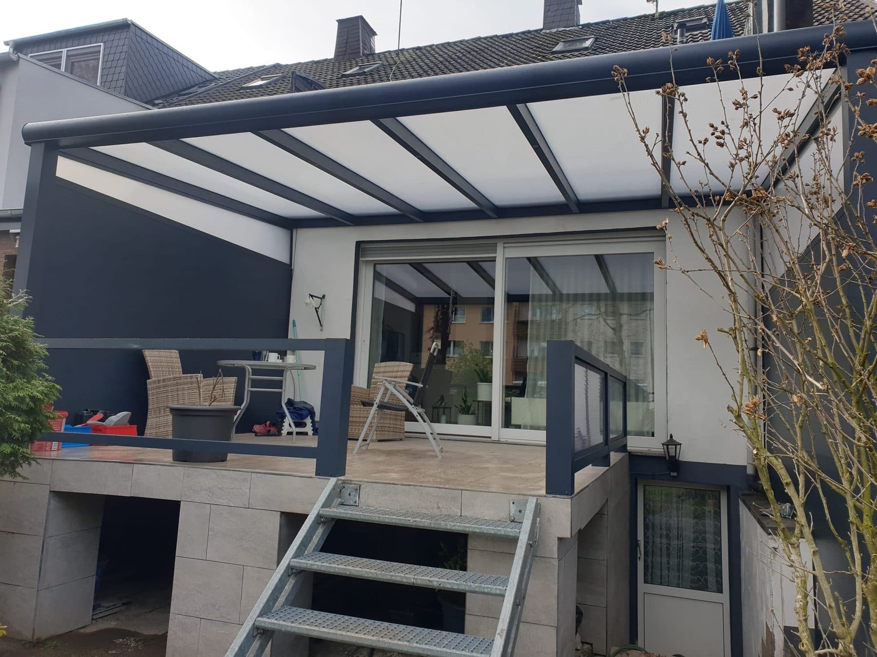 Pergola anthracite à toit polycarbonate opale sur une terrasse surélevée, avec garde-corps assortis et escalier vers le jardin