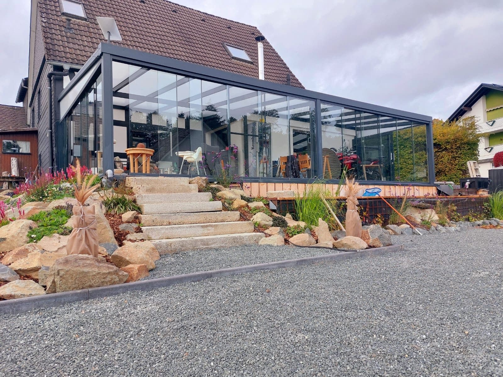 Jardin d'hiver vitré anthracite vu depuis l'allée en gravier, au-dessus du jardin de rocaille